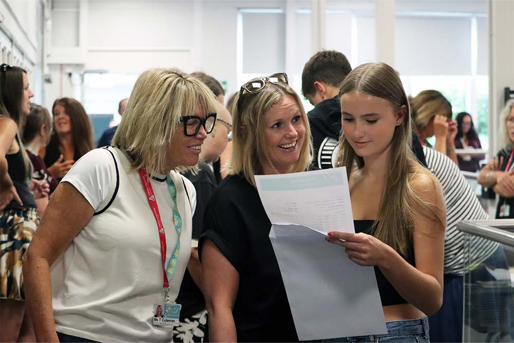 GCSE Results Day 2025 Photo A photo of Ms Coleman standing with a family. A female student is opening her results envelope.