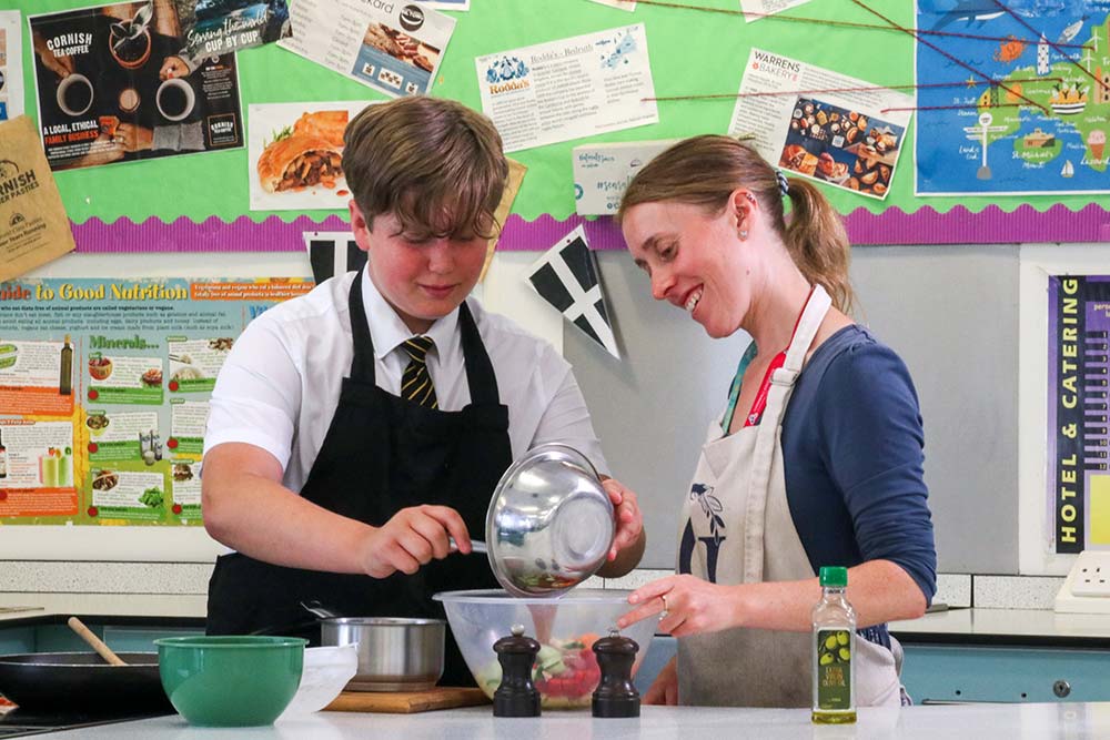 A picture of a male student making a meal with the help of a teacher in a Hospitality and Catering lesson.